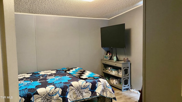 bedroom featuring light hardwood / wood-style flooring, a textured ceiling, and ornamental molding