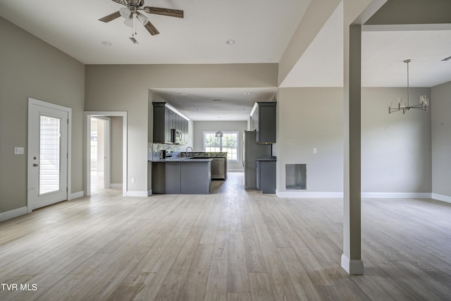 unfurnished living room featuring ceiling fan with notable chandelier, sink, and light hardwood / wood-style flooring