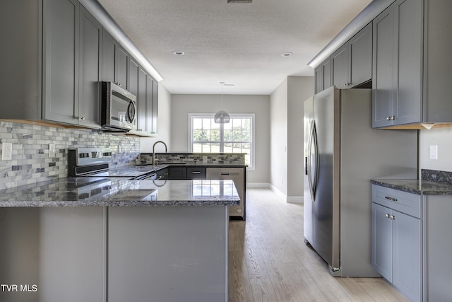 kitchen with kitchen peninsula, appliances with stainless steel finishes, hanging light fixtures, and gray cabinetry