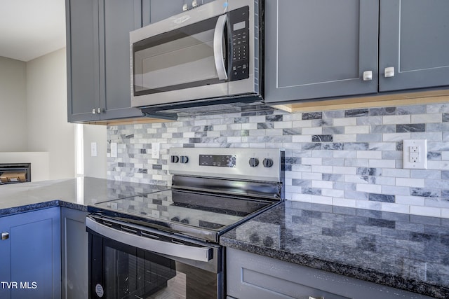 kitchen featuring appliances with stainless steel finishes, backsplash, gray cabinets, and dark stone countertops