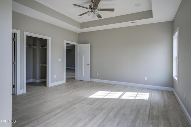 unfurnished bedroom featuring ceiling fan, a closet, a raised ceiling, and light hardwood / wood-style flooring