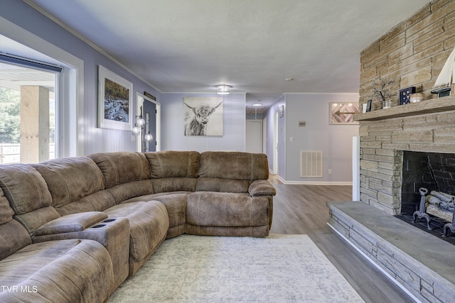 living room featuring wood-type flooring, a stone fireplace, and crown molding