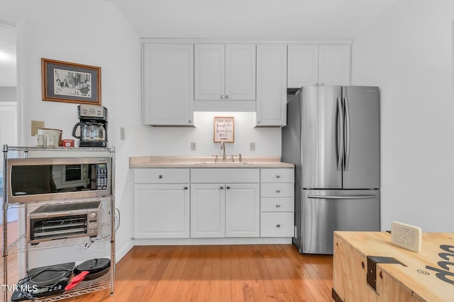 kitchen with stainless steel appliances, sink, white cabinetry, and light wood-type flooring