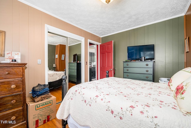 bedroom with wood-type flooring, wooden walls, a closet, and ornamental molding