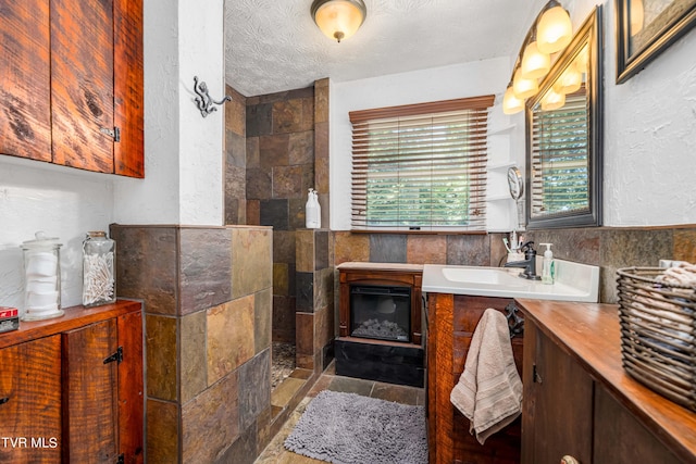 bathroom with vanity, tiled shower, a textured ceiling, and tile walls