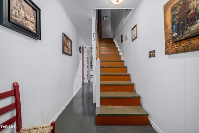 staircase with ornamental molding, wooden walls, and concrete floors