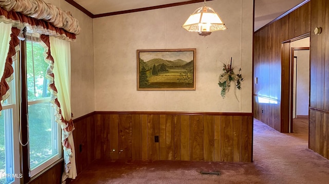 carpeted empty room featuring a healthy amount of sunlight, ornamental molding, and wooden walls