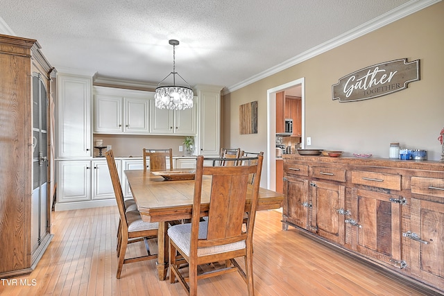 dining area featuring ornamental molding, light hardwood / wood-style flooring, a textured ceiling, and a chandelier