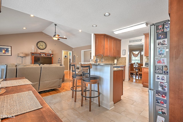 kitchen featuring a breakfast bar area, light stone counters, light hardwood / wood-style floors, lofted ceiling, and kitchen peninsula