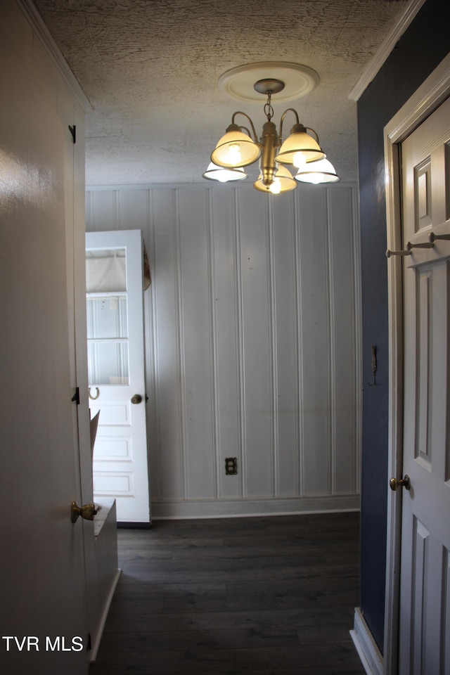 corridor with dark hardwood / wood-style flooring, a textured ceiling, crown molding, and a notable chandelier