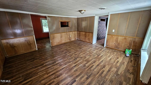 empty room featuring dark hardwood / wood-style flooring, wood walls, and crown molding