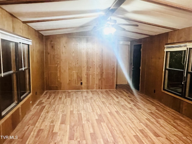 spare room with lofted ceiling with beams, wooden walls, and light hardwood / wood-style flooring