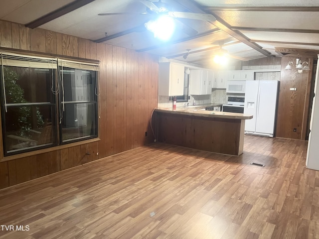 kitchen with kitchen peninsula, white appliances, wooden walls, lofted ceiling with beams, and white cabinetry