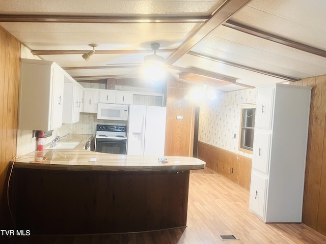 kitchen featuring white cabinetry, kitchen peninsula, wooden walls, and white appliances