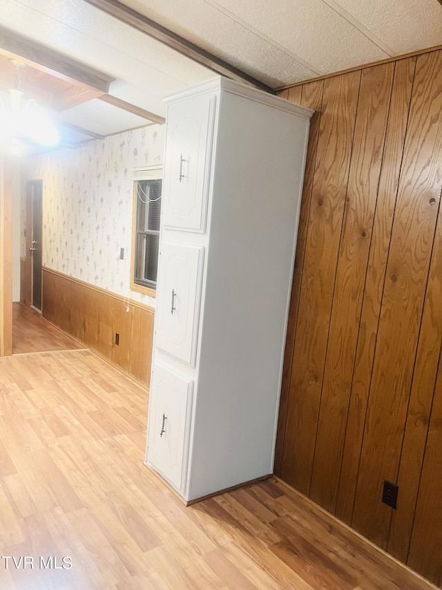 unfurnished room featuring wooden walls, beamed ceiling, and light hardwood / wood-style floors