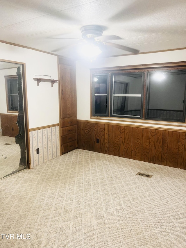 empty room with carpet, ceiling fan, and wood walls