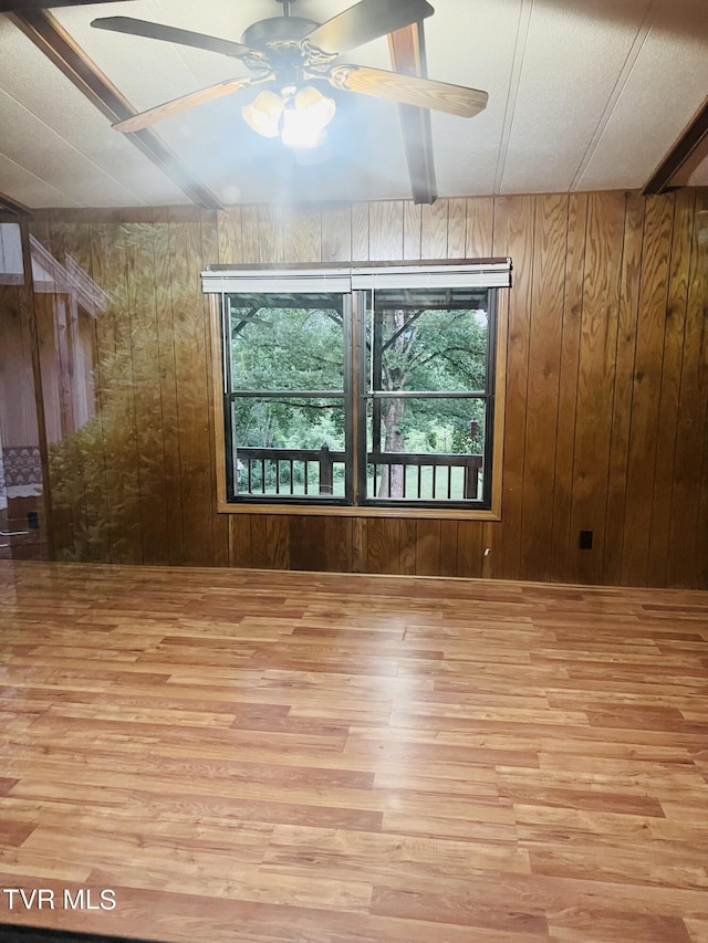 unfurnished room featuring ceiling fan, wood walls, and light hardwood / wood-style floors