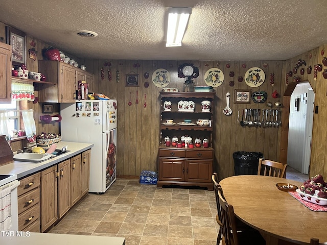 kitchen with sink, light tile patterned floors, a textured ceiling, wood walls, and white fridge