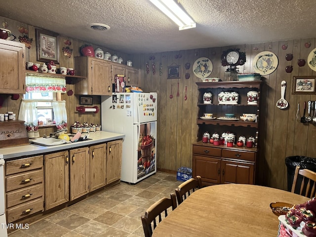 kitchen with light tile patterned flooring, white fridge, wooden walls, and a textured ceiling