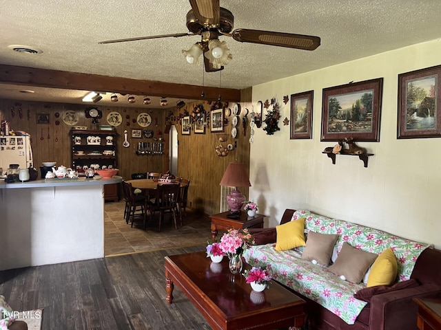 living room with ceiling fan, beamed ceiling, wood-type flooring, and a textured ceiling