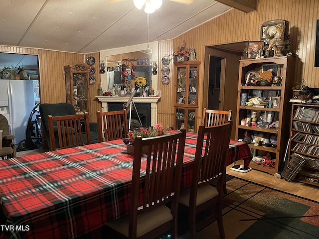 dining space with vaulted ceiling with beams, wooden walls, and a fireplace