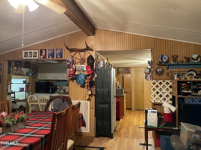 dining space with light wood-type flooring, vaulted ceiling with beams, and wood walls