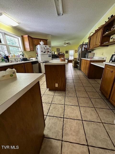 kitchen featuring white refrigerator, ceiling fan, a center island, a textured ceiling, and light tile patterned floors