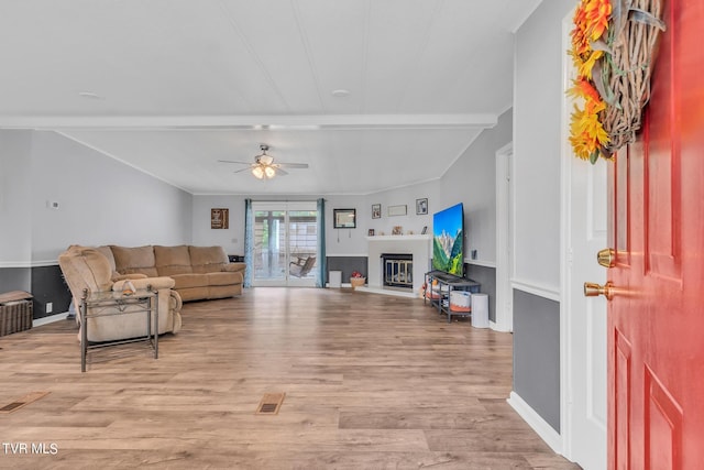 living room featuring ceiling fan, wood finished floors, beamed ceiling, and a glass covered fireplace