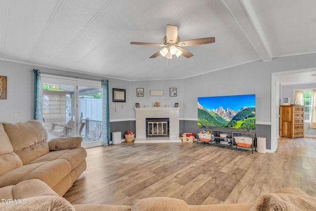 living room featuring light wood-type flooring, ceiling fan, a tile fireplace, lofted ceiling with beams, and ornamental molding