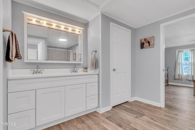 bathroom with a sink, ornamental molding, baseboards, and wood finished floors