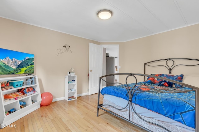 bedroom with ornamental molding, light wood-style flooring, baseboards, and freestanding refrigerator