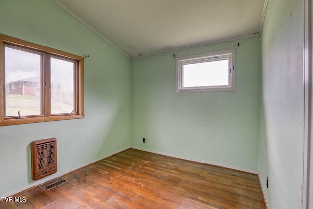 empty room with hardwood / wood-style flooring, vaulted ceiling, heating unit, and ornamental molding