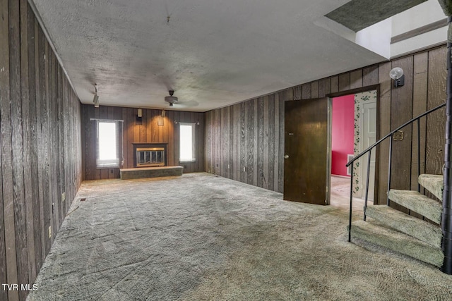 unfurnished living room featuring carpet floors, wooden walls, and a textured ceiling