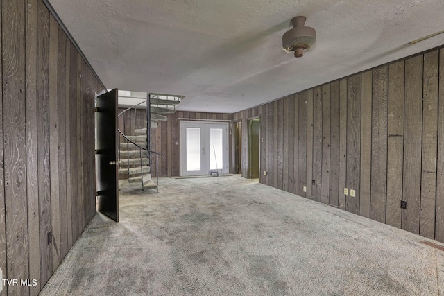 carpeted spare room with wood walls, a textured ceiling, ceiling fan, and french doors