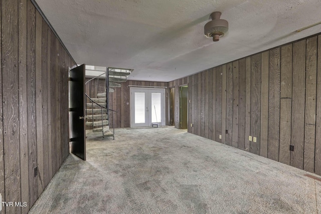 unfurnished living room featuring french doors, wooden walls, carpet floors, and a textured ceiling