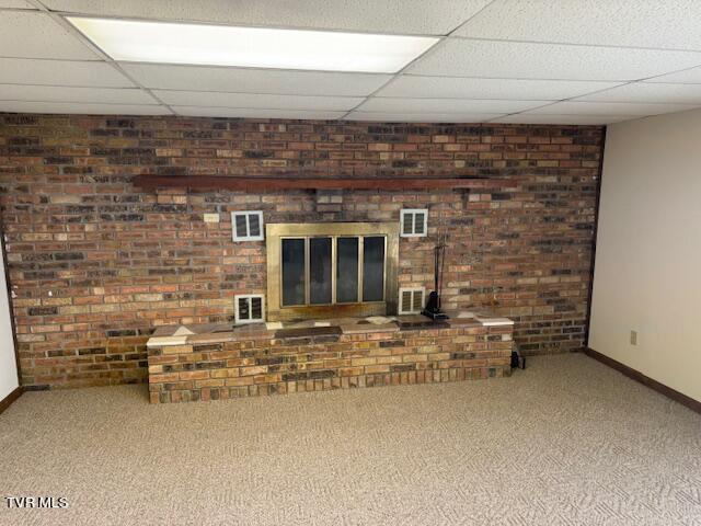 unfurnished living room with baseboards, carpet flooring, a fireplace, and a drop ceiling