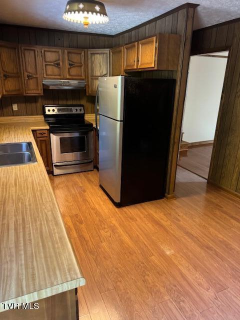 kitchen featuring a textured ceiling, wood walls, sink, appliances with stainless steel finishes, and light hardwood / wood-style floors