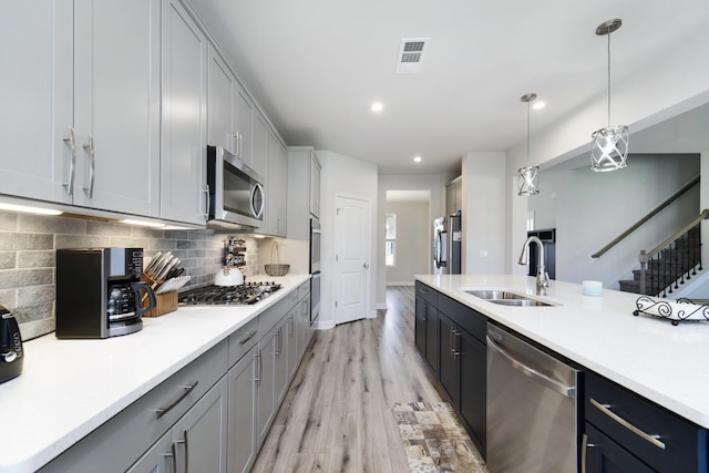 kitchen with tasteful backsplash, hanging light fixtures, sink, appliances with stainless steel finishes, and light hardwood / wood-style flooring