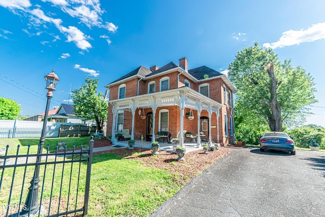 view of front facade featuring a porch, brick siding, fence, a chimney, and a front yard