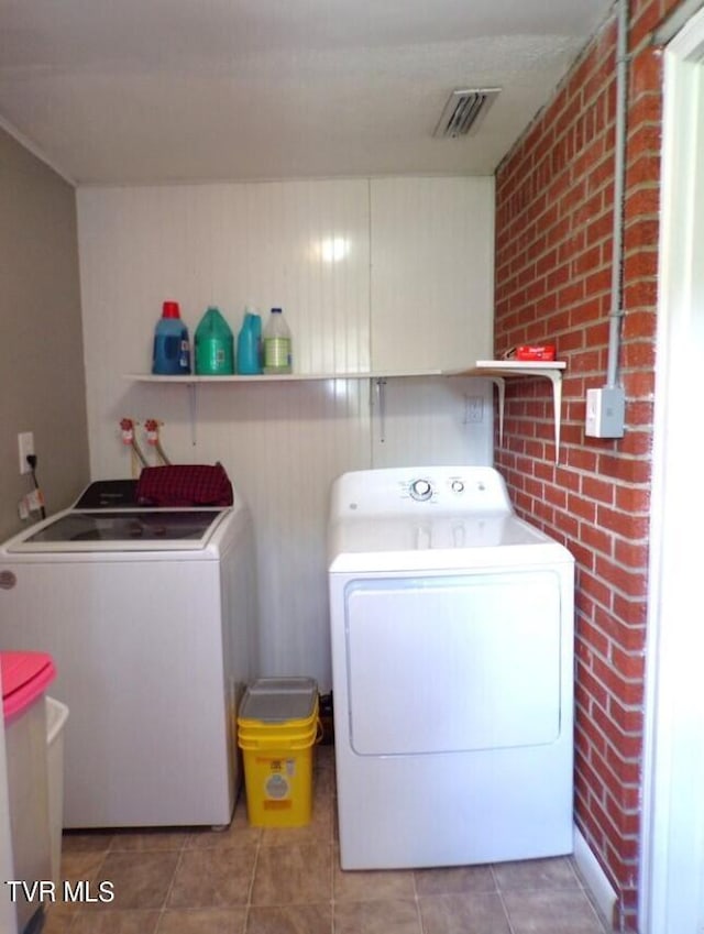 washroom with brick wall, washer and dryer, and tile patterned floors