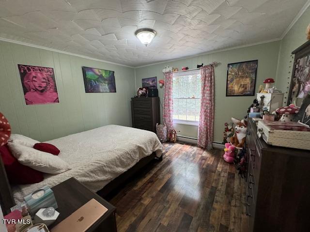 bedroom with ornamental molding, a baseboard heating unit, and dark wood-type flooring