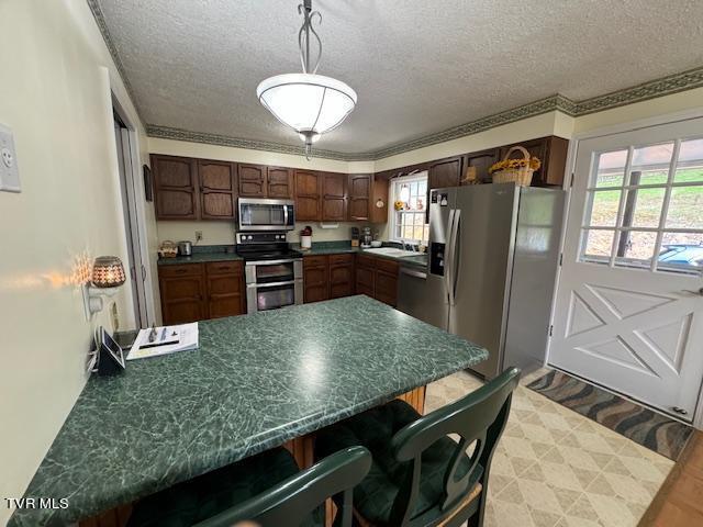 kitchen featuring appliances with stainless steel finishes, decorative light fixtures, a wealth of natural light, and crown molding