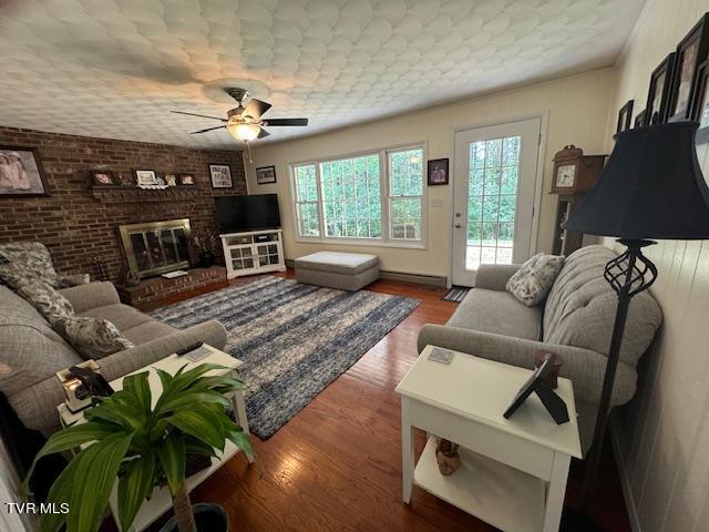 living room featuring dark wood-type flooring, brick wall, ceiling fan, and a brick fireplace