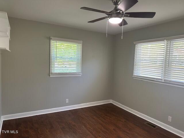 spare room with dark wood-style flooring, visible vents, baseboards, and ceiling fan