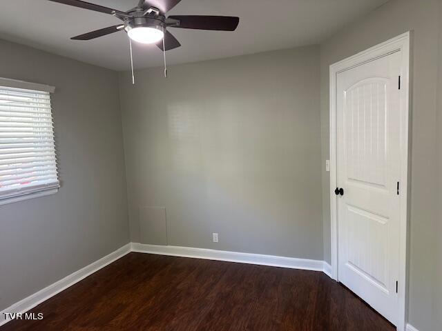 spare room with dark wood finished floors, a ceiling fan, and baseboards