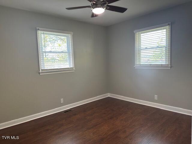 spare room with ceiling fan, visible vents, baseboards, and dark wood-style flooring