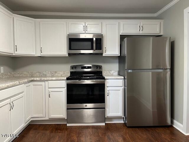 kitchen with white cabinets, ornamental molding, stainless steel appliances, and dark wood-type flooring
