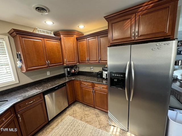 kitchen with appliances with stainless steel finishes, light tile patterned floors, and dark stone countertops