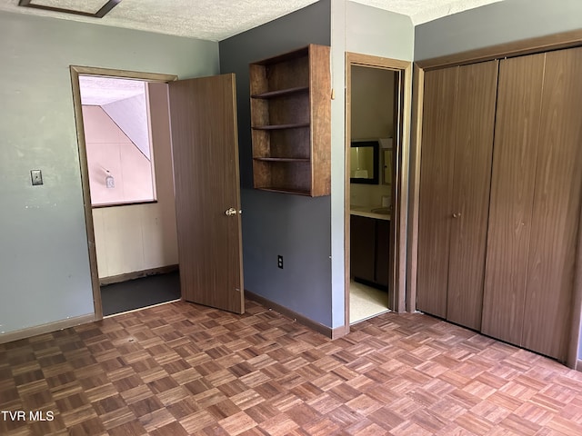 unfurnished bedroom featuring connected bathroom, parquet flooring, and a textured ceiling