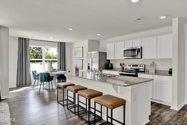 kitchen featuring light stone countertops, a kitchen bar, white cabinetry, stainless steel appliances, and a kitchen island with sink